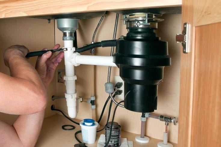 Plumber installing a garbage disposal beneath a kitchen sink in Prescott Valley